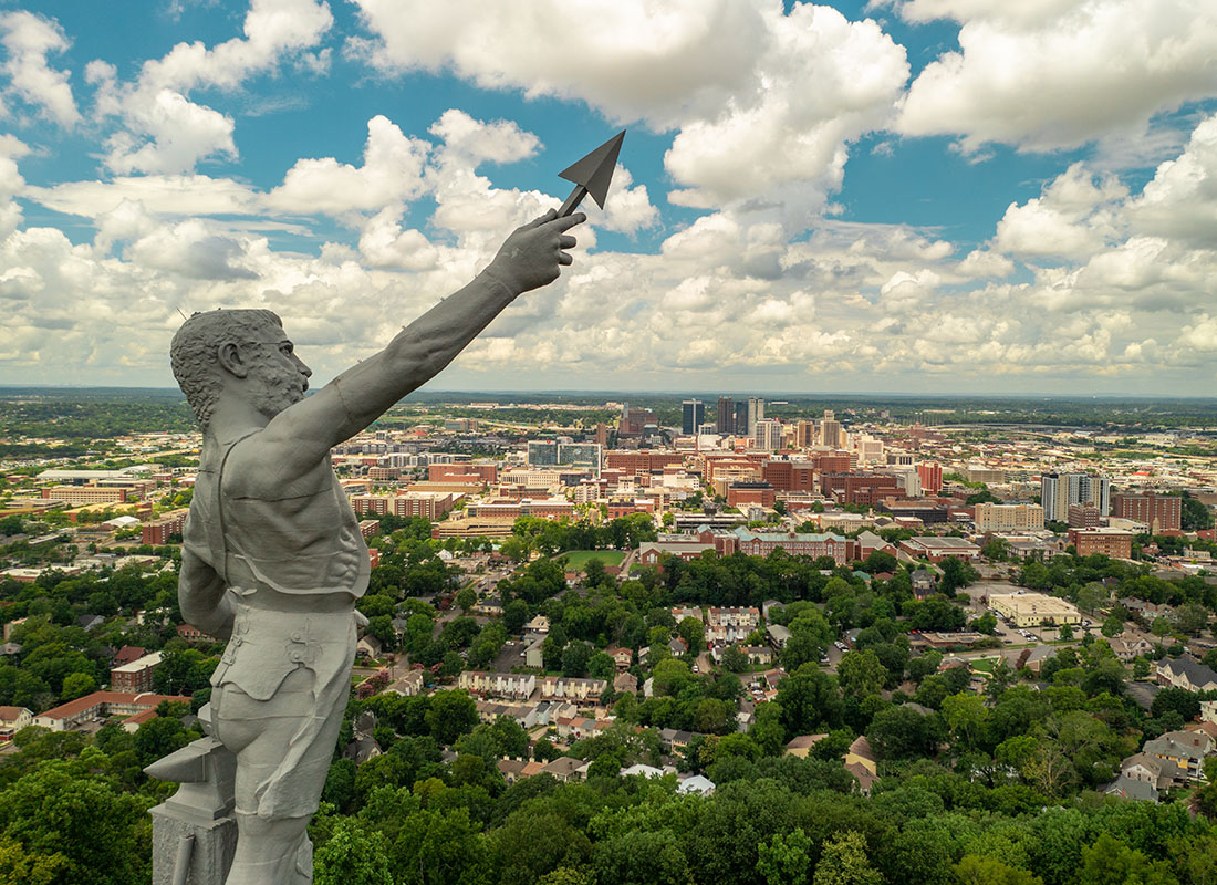 Insurance Solutions - Vulcan Statue in a Park with Views of Buildings and Homes in Birmingham Alabama Against a Cloudy Sky